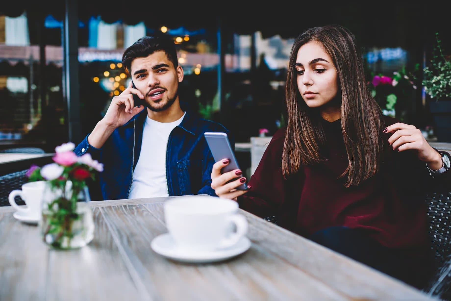 Man talking on phone and woman checking her smartphone while sitting at an outdoor cafe.