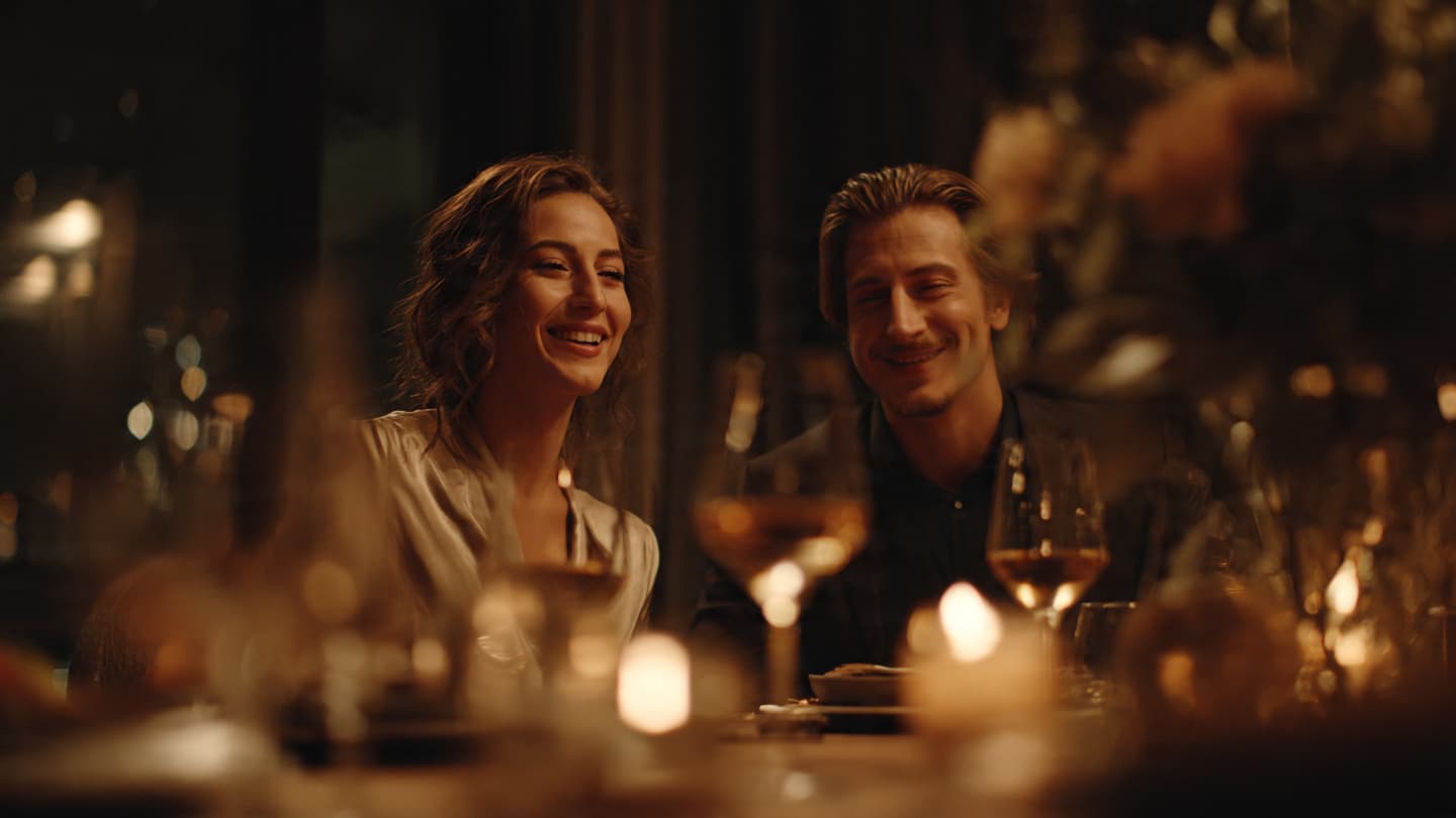 Smiling couple enjoys a romantic candlelit dinner with wine in a warm and elegant setting.